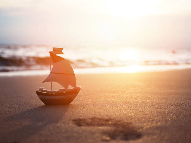 istock Silhouette small boat toy on sand at sunset beach 1159365803