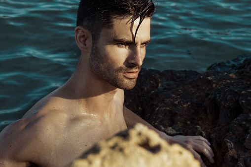Strong face male model on the nature background with sand stones and water on the beach on the sunset