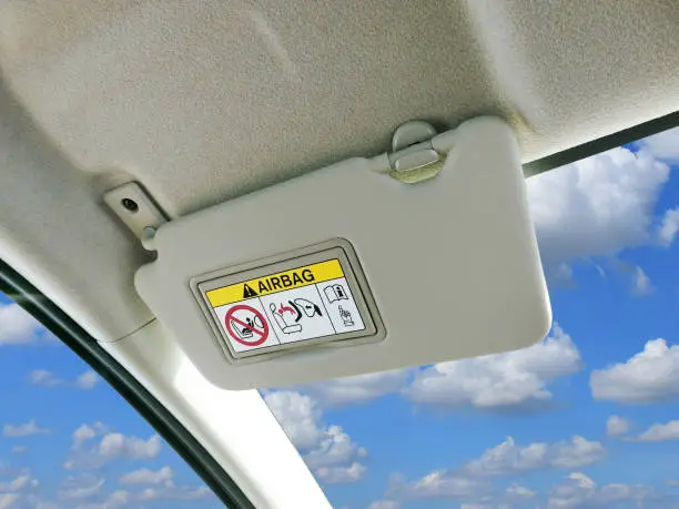 Car sun visor and warning signs of airbag system in car with sky and clouds as a backdrop.