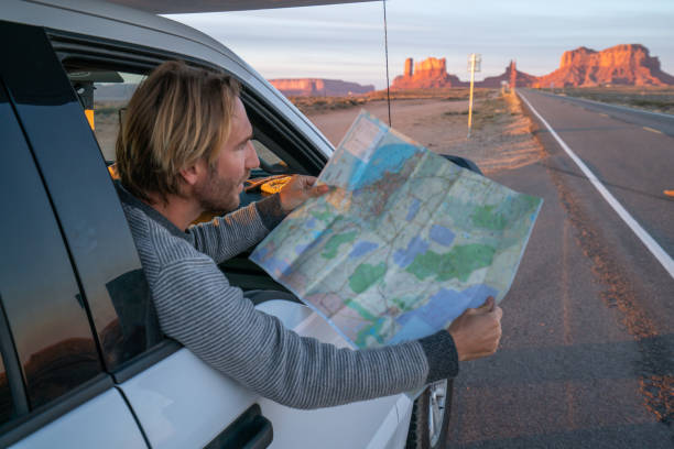 istock Road trip concept; Young man inside campervam looking at road map for directions exploring national parks and nature ready for adventure. 1159368417