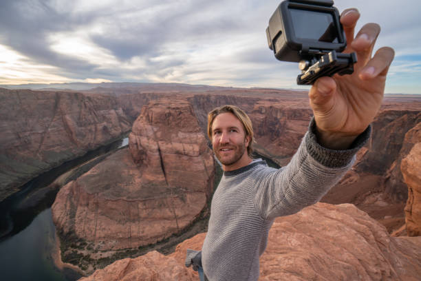 Young man taking selfie with action camera at the horseshoe bend in Arizona, USA View of a man taking selfie picture at the famous horseshoe bend by the Colorado river at sunset, beautiful dramatic colourful sky. people travel concept horseshoe bend river stock pictures, royalty-free photos & images