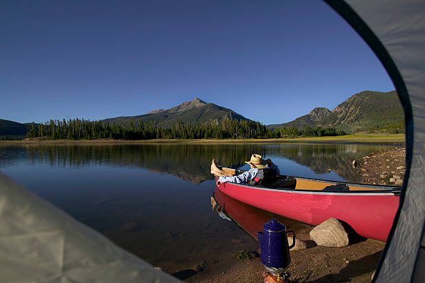 istock Man Relaxing in Canoe on Mountain Lake Framed by Tent 115936855