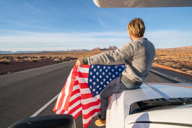 roadtrip-konzept; junger mann sitzt auf wohnmobil mit amerikanischer flagge - navajo national monument stock-fotos und bilder