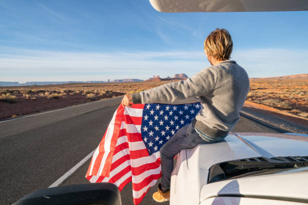 concepto de viaje por carretera; joven sentado en rv sosteniendo la bandera estadounidense - navajo national monument fotografías e imágenes de stock