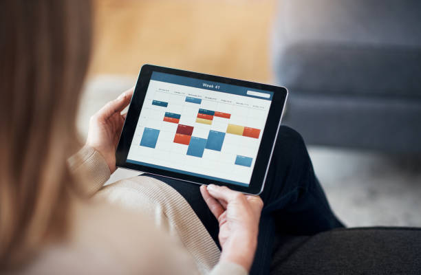 Making sure I have no colliding appointments Cropped shot of an unrecognizable woman sitting and viewing a timetable on a tablet in her living room online calendar stock pictures, royalty-free photos & images