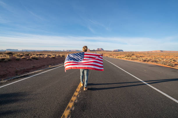 istock Man on road holding American flag 1159369899