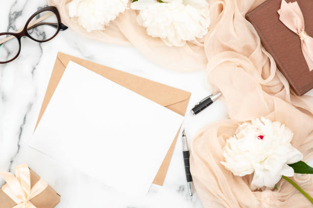 istock Top view blank wedding invitation card and craft paper envelope on marble background with white peony flowers and pastel beige scarf. Minimal flatlay style composition, concept of wedding and marriage 1159369996