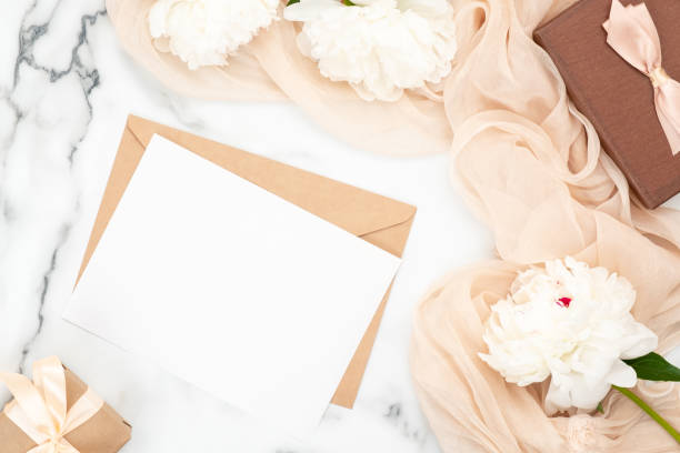 istock Top view blank wedding invitation card and craft paper envelope on marble background with white peony flowers and pastel beige scarf. Minimal flatlay style composition, concept of wedding and marriage 1159370007