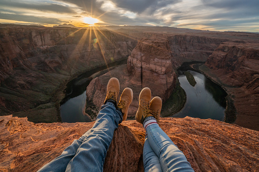 Personal perspective of couple relaxing on top of horseshoe bend in Arizona; feet view; 
People travel vacations relaxation concept