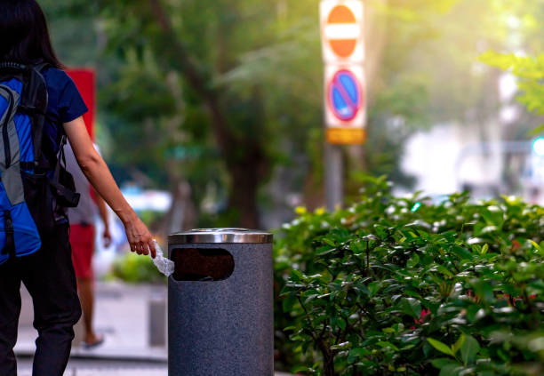Woman hand throwing twisted empty water bottle in recycle bin. Gray plastic recycle bin. Backpacker discard bottle in trash bin. Waste management. Plastic bottle garbage. Reduce and reuse plastic.
