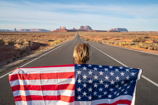 istock Man on road holding American flag 1159371560