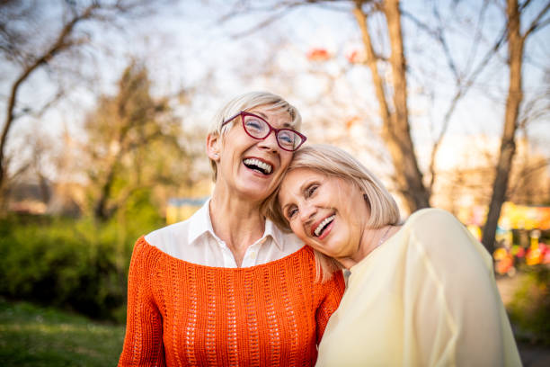 zwei seniorinnen lachen im park - women mature adult smiling mature women stock-fotos und bilder