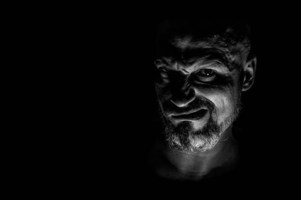 istock Face with a bearded man grimace against a dark background with sharp shadows. Comedic, fabulous villain or negative character conception with copy space. 1159373453