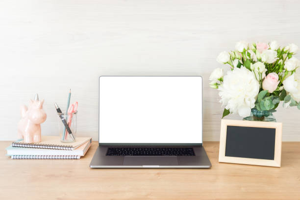 Home office desk table with laptop computer with blank white screen, supplies, picture frame, feminine accessories and flowers bouquet on wooden surface. Stylish woman workplace concept.