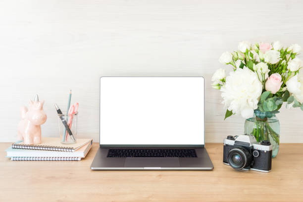 istock Workspace laptop computer with blank white screen and office supplies on office workplace. Feminine desk table with laptop, flowers, film camera, unicorn, books on wooden surface. Copy space 1159375479