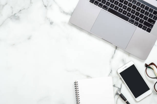 istock Business composition with laptop computer, paper notepad, glasses, smartphone with blank screen on white marble background. Concept of woman workspace. Top view with copy space for text. 1159376146