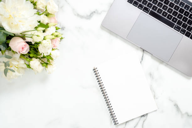 istock Flat lay home office desk. Female workspace with laptop computer, flowers, paper notepad on white marble surface. Top view feminine background. Business woman workplace concept. 1159376152