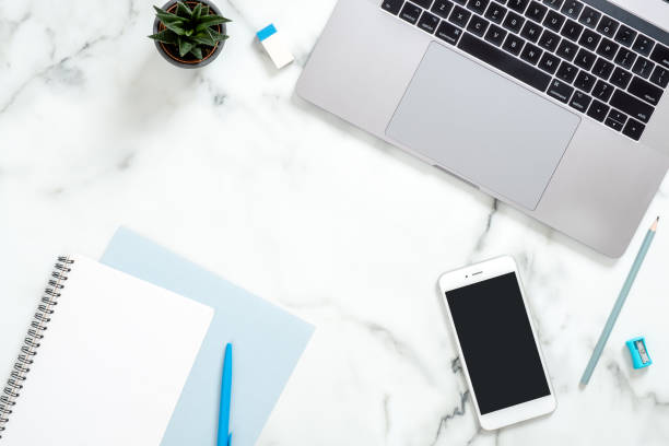 istock Office desk table with laptop computer, smartphone with blank screen, diary, blue stationery, succulent plant on white marble surface. Flat lay, top view feminine background. Business woman workspace 1159376155