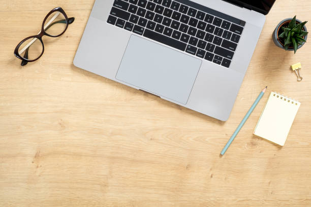 istock Modern wooden office desk table with laptop computer, paper notepad, succulent plant, glasses. Top view with copy space, flat lay. Feminine workspace concept. 1159376170