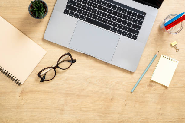 istock Modern wooden office desk table with laptop computer, paper notepad, succulent plant, glasses. Top view with copy space, flat lay. Feminine workspace concept. 1159376171