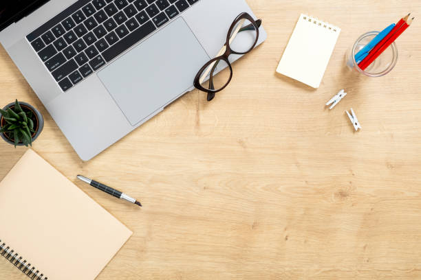 istock Wood office desk table with laptop computer, glasses, paper notepad, pen, stationery. Minimal flat lay style composition with copy space, top view. Stylish home office desk concept. 1159376174