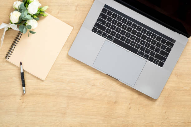 istock Modern wooden office desk table with laptop computer, paper notepad, pen, succulent plant, bouquet of roses flowers. Minimal flat lay style composition with copy space, top view. Feminine workspace. 1159376177