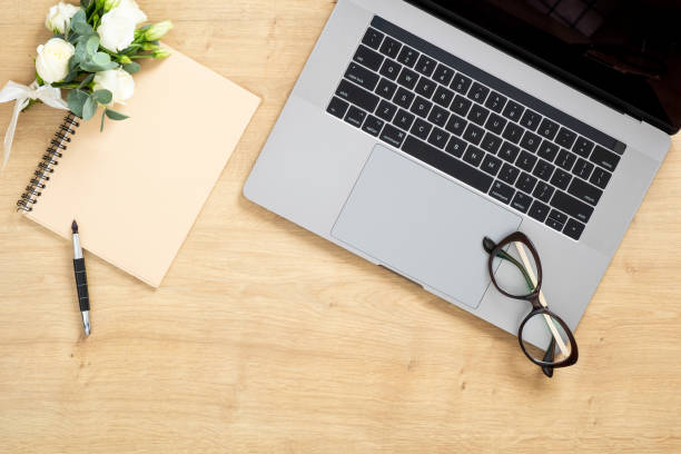 istock Modern wooden office desk table with laptop computer, paper notepad, pen, succulent plant, bouquet of roses flowers. Minimal flat lay style composition with copy space, top view. Feminine workspace. 1159376178