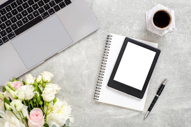 istock Office desk table with laptop computer, blank copy space mockup screen tablet, flowers, cup of coffee and supplies on concrete stone background. Top view with copy space, flat lay. Feminine workspace 1159376230