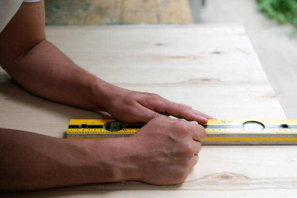 istock Carpenter marking straight line on plywood sheet using spirit level in carpentry workshop. Measuring, drawing line, DIY concept. 1159376348