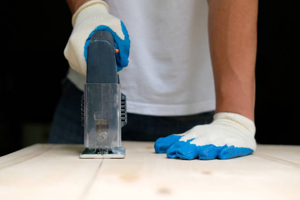 istock Carpenter in gloves using electric jig saw in workshop. Front view. Carpentry concept. 1159376479