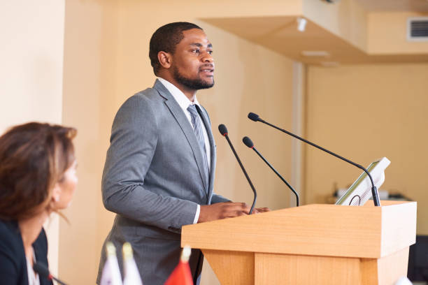 Man by tribune Young African-american male speaker talking in microphone while making speech by tribune for business colleagues or delegates politician stock pictures, royalty-free photos & images