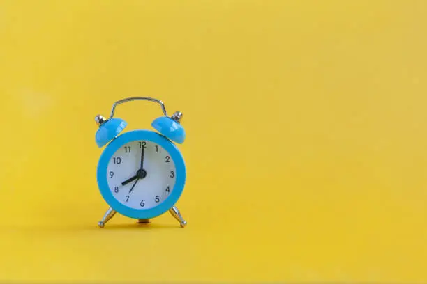 Photo of Blue alarm clock on yellow background. Minimalism. Contrast concept.