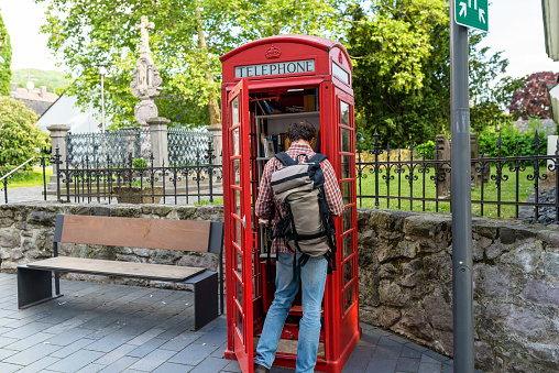 Konigswinter, Germany - 23 May 2019. A red telephone booth for the free exchange of books. A man looking at a book in a telephone booth.