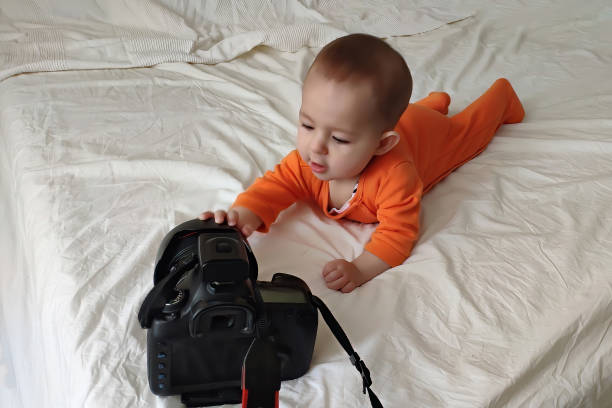 A small baby infant plays with a big camera and lying on the bed