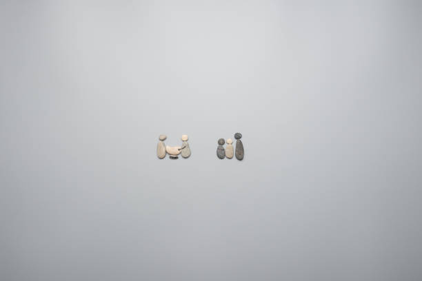 Two family units made of pebbles. Over grey background, with copy space.