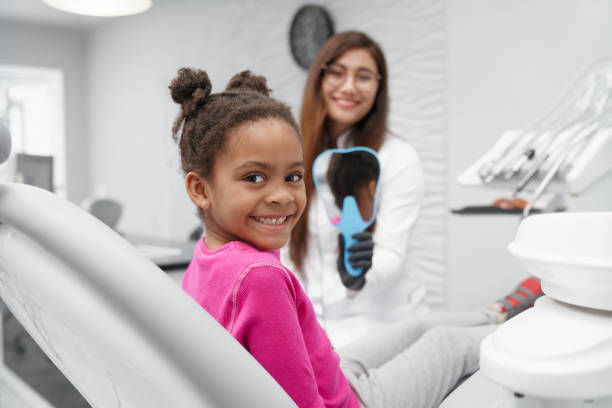 カメラを見て、笑顔の歯科医の椅子に座っている女の子 - dental implant dental hygiene dentures prosthetic equipment ストックフォトと画像