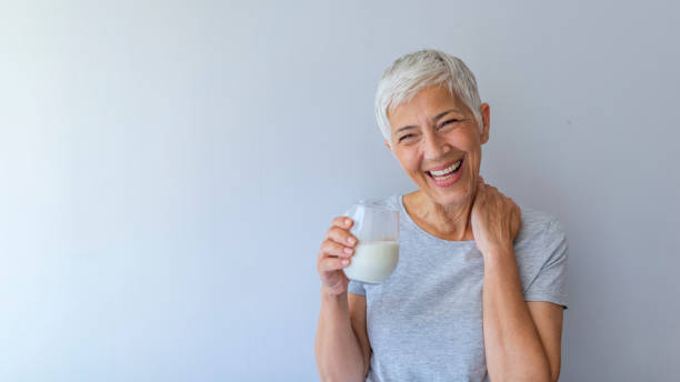 Senior woman drinking from a clear glass full of milk Cheerful mature woman having fun while drinking milk. Senior woman drinking from a clear glass full of milk. Woman in her golden age. Smiling, beautiful senior lady drinking a glass of milk 60 69 years stock pictures, royalty-free photos & images