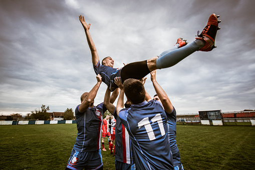 Happy sports team holding their teammate high up while celebrating their success after the match. Copy space.