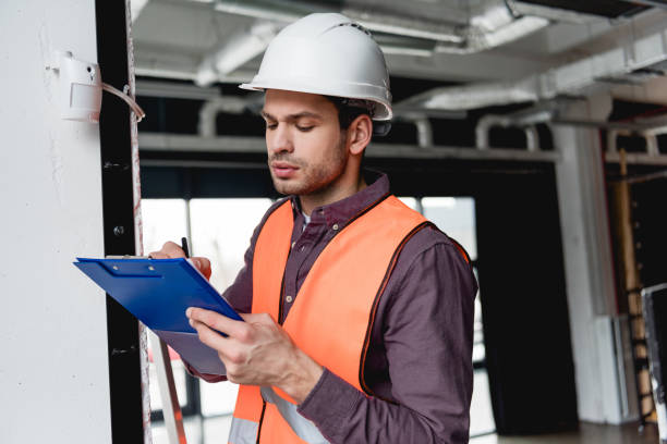 istock handsome fireman in helmet standing near fire alarm while looking at clipboard 1159389001