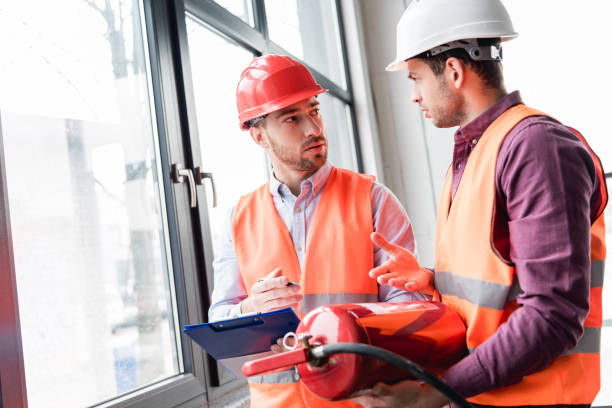 istock fireman in helmet looking at coworker while talking and holding red extinguisher 1159389007