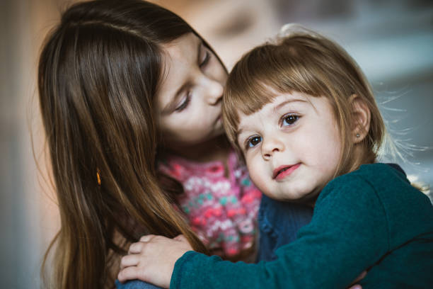 Cute little girl enjoying in a kiss by her older sister at home.
