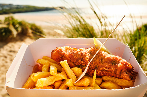 box of Fish and Chips at Fistral Beach, Newquay, Cornwall on a sunny June evening.