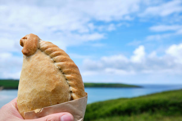 istock Hand holding a Cornish Pasty overlooking Crantock Beach, Newquay, Cornwall on a sunny June day. 1159391680