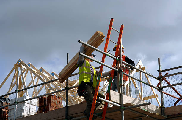 Low view of two construction workers on top of house frame A pair of roofers working on a construction site in Manchester, England. No sharpening in camera or pp. scaffolding stock pictures, royalty-free photos & images