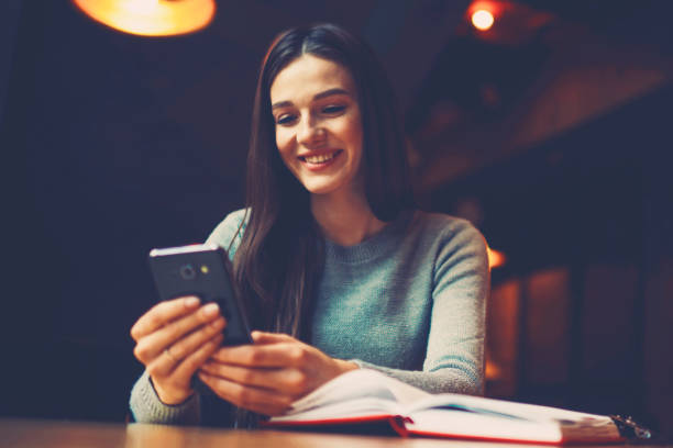 istock Cheerful blogger reading received sms message with good news from operator on digital smartphone sitting at opened literature book in coworking space.Positive student doing shopping online on cellular 1159396205