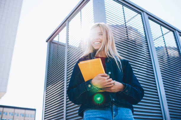 istock Good looking cheerful smart female student dressed in casual clothes sincerely laughing while strolling at sunny street.Attractive smiling blonde teenager having fun at urban setting during walk 1159398951