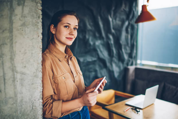 istock Thoughtful casual dressed female blogger pondering on creative ideas for developing own website holding modern smartphone.Contemplative hipster girl thinking on plans while standing in coworking 1159399191