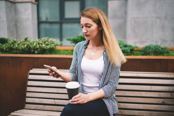 istock Hipster girl sending text messages and checking notification at smartphone while enjoying coffee break, serious female student holding contemporary mobile phone and blogging at leisure outdoors 1159400070