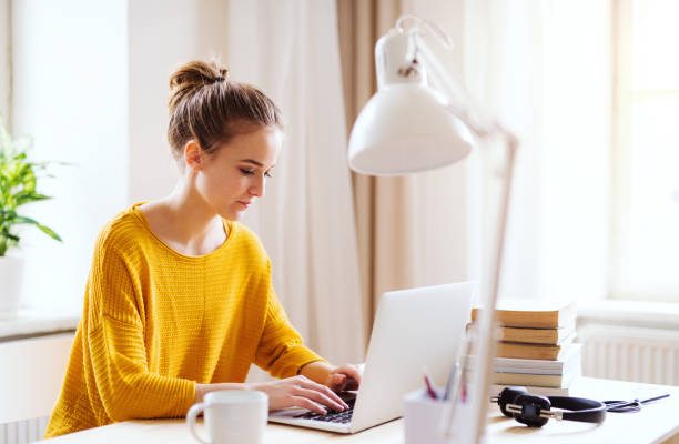 una giovane studentessa seduta al tavolo, che usa il laptop quando studia. - furniture internet adult blond hair foto e immagini stock