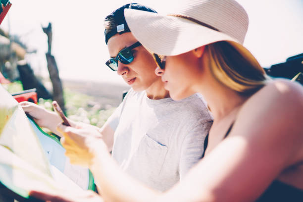istock Male and female tourist reading map and using navigation app on smartphone for searching route sitting in rental car, couple of travelers browsing information on cellphone for getting to destination 1159402602